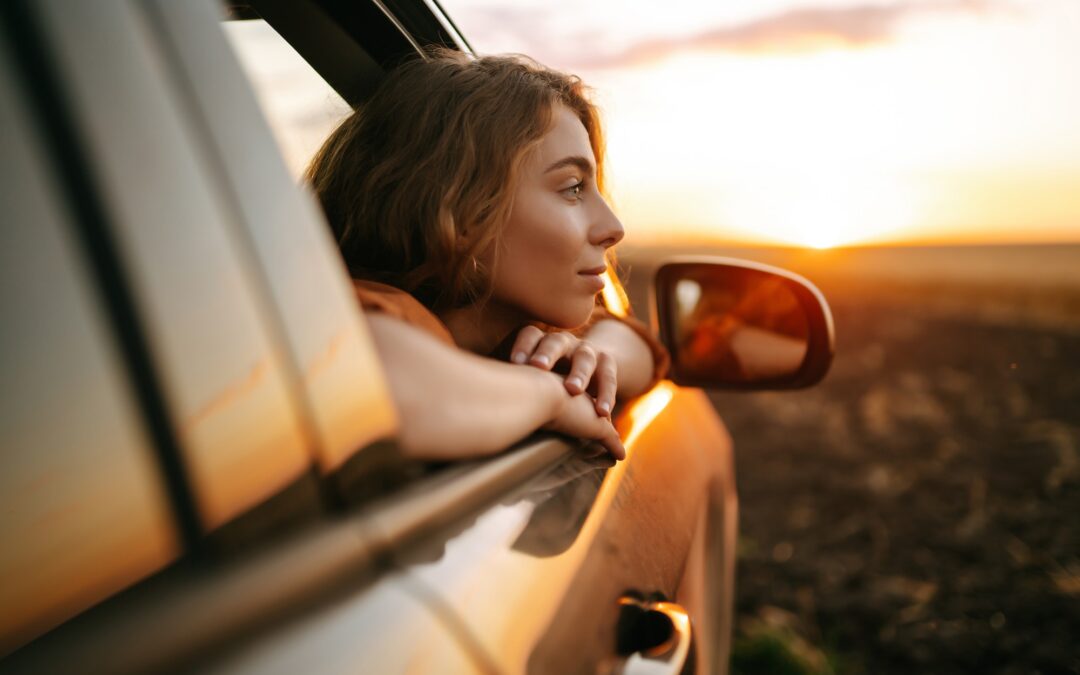 Happy woman outstretches her arms while sticking out car window. Lifestyle, travel, tourism, nature.