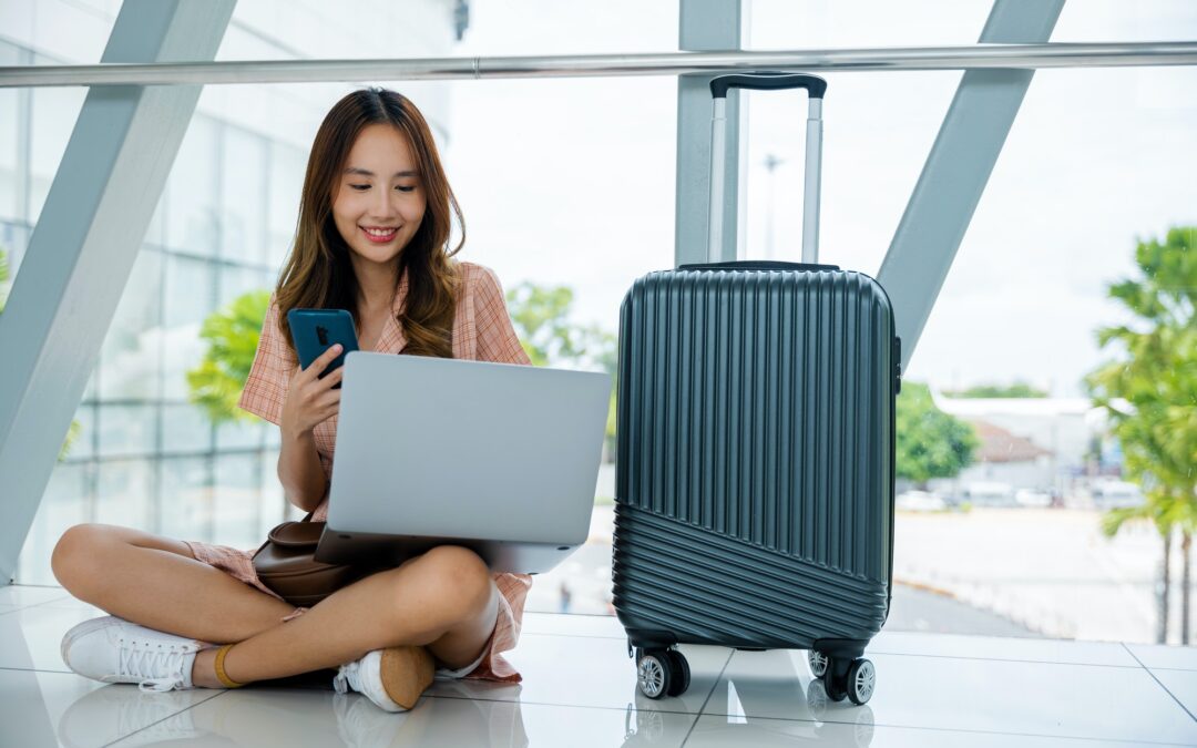 woman sitting on the airport floor, typing on her phone and laptop